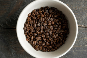 Bowl filled of fresh arabica or robusta coffee beans on a wooden table.