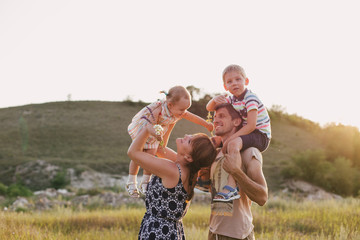 Happy family of young parents and their little children walking in a field at sunset.