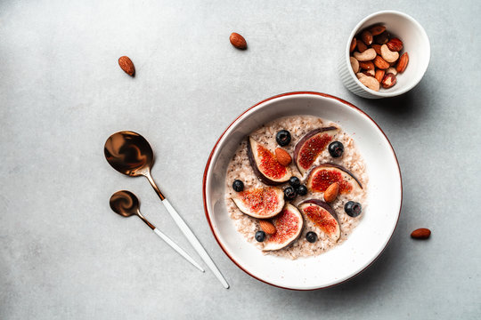 Healthy breakfast set. Oatmeal with nuts, fresh figs and blueberries in bowl on light background, top view, copy space