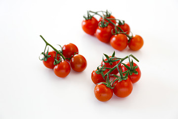 Branch of beautiful juicy organic red cherry tomatoes on white background. Top view of shiny polished glossy vegetables. Clean eating concept. Vegetarian vegan summer detox diet. Copy space, flat lay.