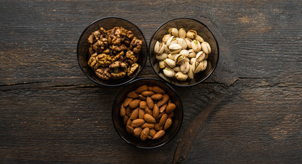 Fototapeta na wymiar Almond, pistachio and walnut in a small plates which standing on a black table. Nuts is a healthy vegetarian protein and nutritious food.