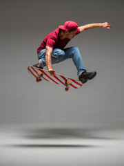 Cool young guy skateboarder jumps on skateboard in studio on grey background. Photography about...