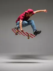 Poster Im Rahmen Cool young guy skateboarder jumps on skateboard in studio on grey background. Photography about skateboarding tricks © Georgii