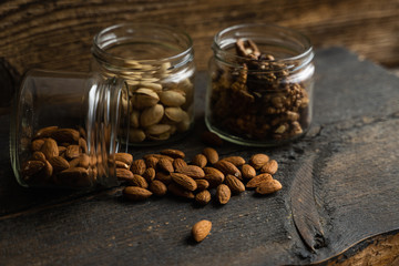 Almonds scattered on the wooden vintage table from a jar. Almond is a healthy vegetarian protein nutritious food. Almonds on rustic old wood.