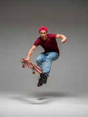 Fototapeta na wymiar Cool young guy skateboarder jumps on skateboard in studio on grey background. Photography about skateboarding tricks