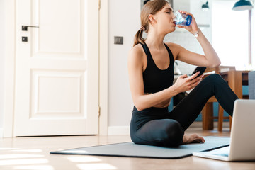 Attractive tired young fitness woman drinking water