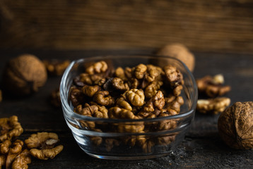 Walnut in a smale plate with scattered shelled nuts and whole nut which standing on a wooden vintage table. Walnuts is a healthy vegetarian protein nutritious food. Walnut on rustic old wood.