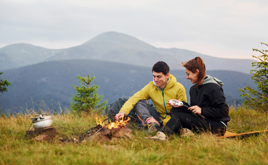 Fototapeta premium Couple with marshmallow near campfire. Majestic Carpathian Mountains. Beautiful landscape of untouched nature