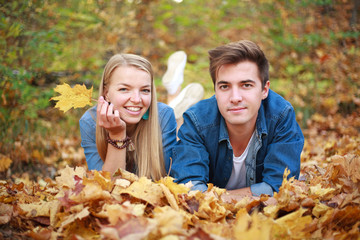 Young couple in love, a guy and girl having fun in fallen leaves in autumn forest together