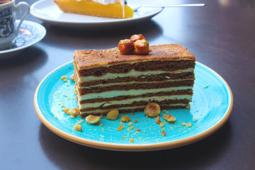 Delicious piece of chocolate cake with cream and nuts on a blue plate on a table in a cafe