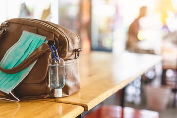 Mini portable alcohol gel bottle to kill Corona Virus(Covid-19) hang on a leather shoulder bag of a woman with a surgical mask on table at cafeteria.New normal lifestyle.Selective focus on alcohol gel