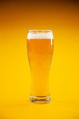 Glass of beer with foam on orange background