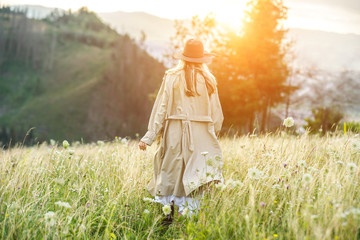 Happy woman in Hat and trench coat enjoying sunset stay on the green grass.