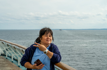 Photo of an Asian woman in her 50s makes a v-sign. Blue ocean and sky background