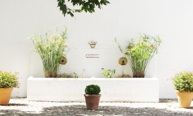 Fontaine zen en pierre blanche , décorée de roseaux, de fleurs, adossée à un mur d'une place de la ville de Ronda en Espagne
