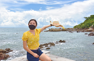 Young woman cheerful the beach under the sun wearing the protective face mask due to coronavirus, new normal concept.