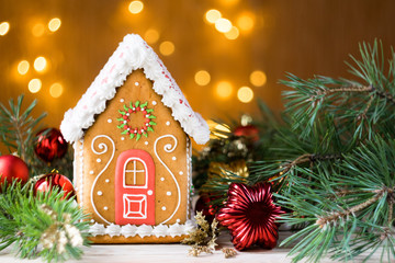 Beautiful gingerbread house with pine branches and new year's toys, lights in background, horizontal orientation, copyspace, selective focus