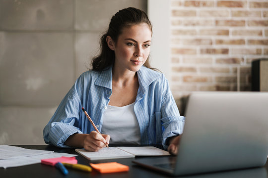 Photo of girl writing down notes using laptop while sitting ar table