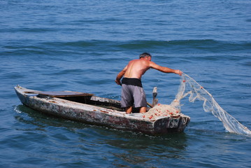
fisherman on a wooden rowboat casting nets into the water