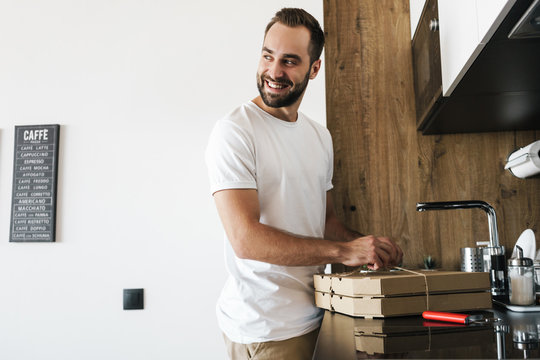 Image of young happy guy smiling and opening boxes with pizza