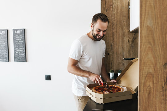 Image of young happy guy smiling and cutting pizza