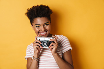 Image of laughing african american woman taking photo on retro camera