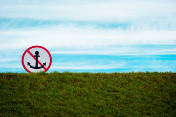 Sign for water vessels "Do not drop anchor" against the blue sky, set on a grassy hill by the sea. Landscape photo with a free space for your text