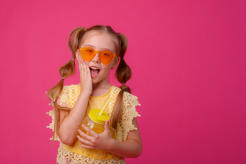 a little girl in sunglasses with a cocktail on a pink background