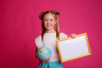 Portrait of a girl holding a globe in her hands and an empty frame, smiling place for text Studio on a pink background