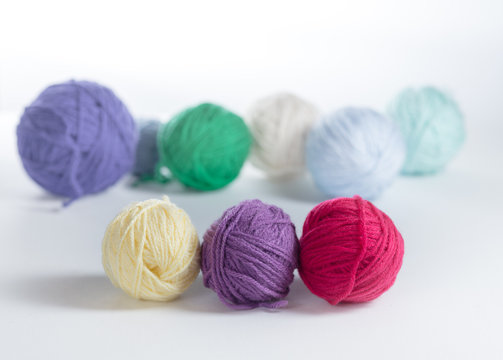 Three small balls of yarn in a row on a light surface, with other colored balls of yarn in the background.  Knitting or crochet materials up close with side light.