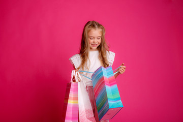 a little Girl with a lot of shopping bags on a pink background in the Studio, happy