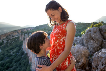 Portrait of a smiling boy hugging mom, a woman with a child on top of a mountain.
