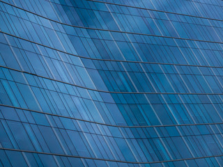 Abstract view of curved glass window panels on a commercial or corporate style building.  Deep dark blue color on reflective diagonal surface.