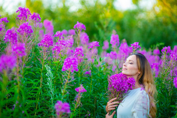 A young woman stands in a field of Ivan's tea and holds a bouquet of purple flowers. Spring mood concept