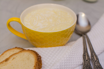 Milk noodle soup in a yellow ceramic bowl and two slices of white bread with sesame seeds on a gray table.