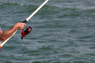 Primer plano de pescador con su caña de carrete pescando en el mar.