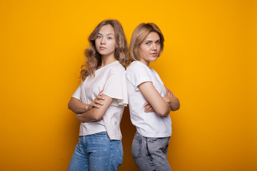 Cute blonde women posing back to back on a yellow studio wall with crossed hands