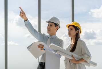 Asian Construction engineers of man and woman are looking and checking work at construction site with blueprint in hand at construction site. Industrial concept.
