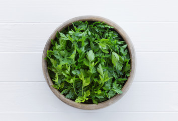Parsley in a wooden bowl. Fresh sprigs of parsley from the garden on a white wooden background. Fragrant seasoning. Cuisine ingredient, condiment.