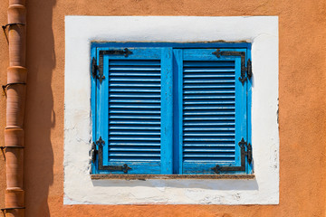 Blue wooden window on a white and orange wall, colorful houses in Salina, typical building of the Aeolian Islands, Sicily, Italy.
