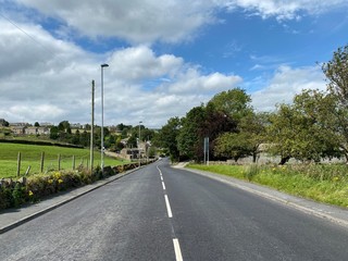 Fototapeta na wymiar Main road, leading down into Keelham, with dry stone walls, fields and trees near, Denholme, Bradford, UK