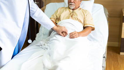 Female doctor comforting or giving psychological help and holding hand of senior man patient in recovery room at hospital