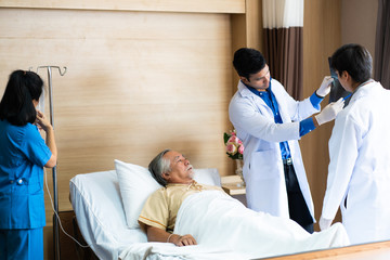 Middle aged Asian male doctor and nurse talking about the illness of the senior elderly man patient on the hospital bed