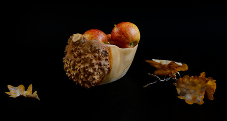 autumn leaves and apples in a wooden vase on a black background