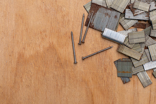 Background With Copy Space. Top View Of Four Nail And Group Of Nail Strip (for Nail Gun / Staple Gun) On Wooden Board For Carpentry And Woodworking Projects. Many Sizes Of Nails. Some Nail Are Rusted.