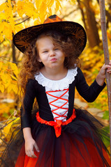 a girl dressed as a little witch on Halloween in a Park with a broom near yellow leaves    
