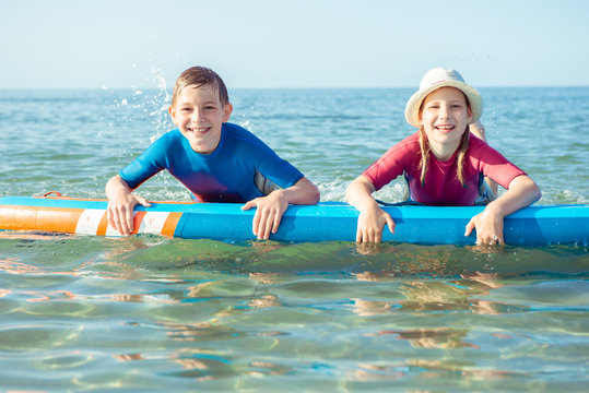 Two happy siblings teen children in neoprene suits having fun  with sup board in Baltic sea