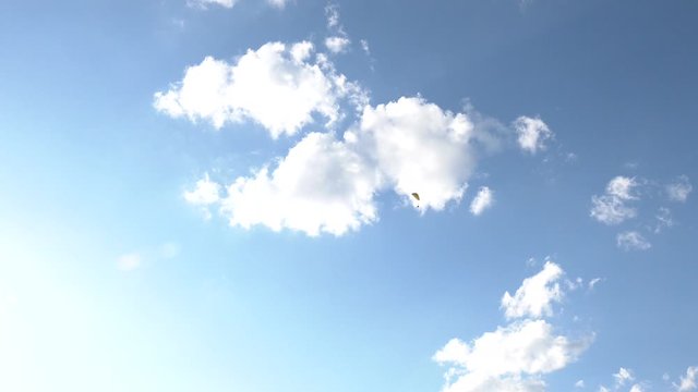Paraglider flying over fields in sunny day. Paraglider in the blue sky.  High altitude. Silhouette of paraglide flying in the sky with clouds in a light of sunrise. 
