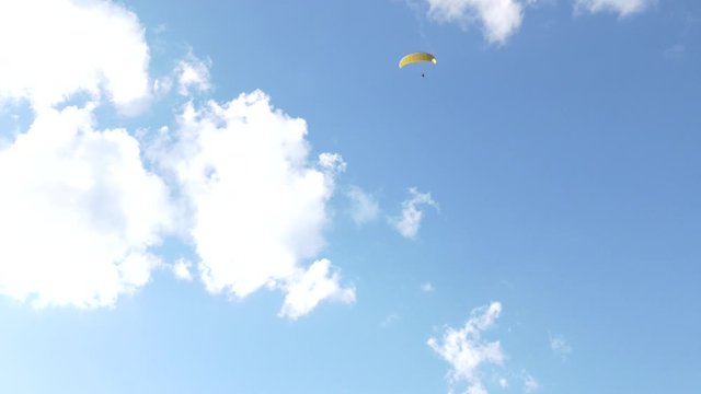 Paraglider flying over fields in sunny day. Paraglider in the blue sky.  Silhouette of paraglide flying in the sky with clouds in a light of sunrise. Paraglider flying in the air stream.
