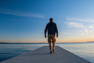 Man in hoodie and short cargo pants on dock, sea horizon in background, island od Pag, Adriatic...